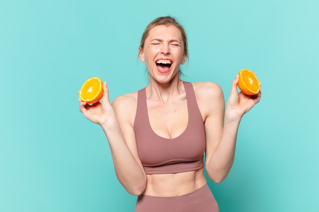 Young pretty sport woman angry expression and holding an orange