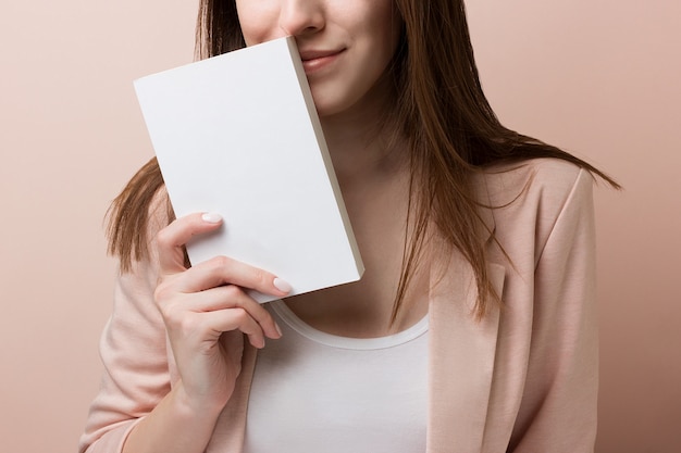 Young pretty student smiles and holds empty book isolated on pink background