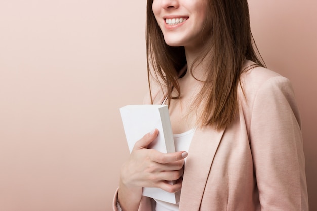 Young pretty student smiles and holds empty book isolated on pink background