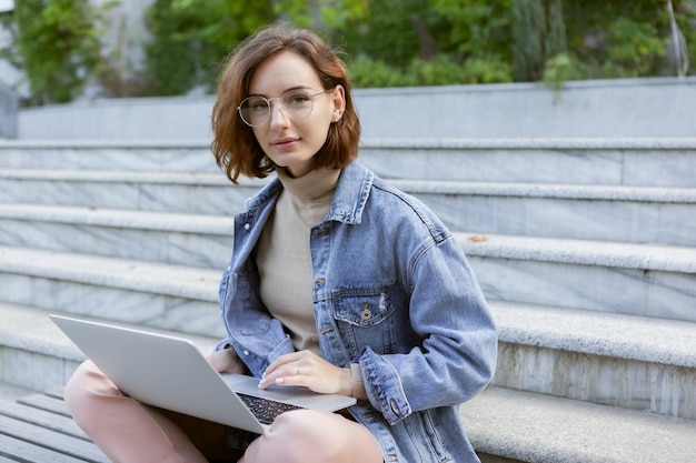 Young pretty student woman sitting with laptop Caucasian girl working or study with notebook outdoors