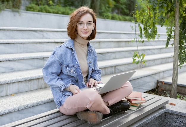 Young pretty student woman sitting with laptop Caucasian girl working or study with notebook outdoors