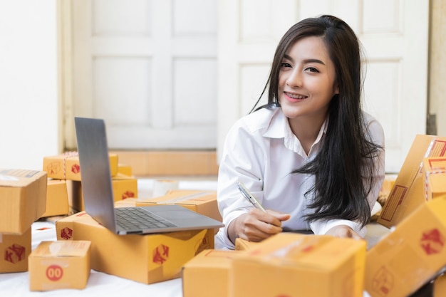 Young pretty teenage work at home write note on parcel box. Asian Women happy after new order from customer, online shopping SME entrepreneur or freelance working concept.