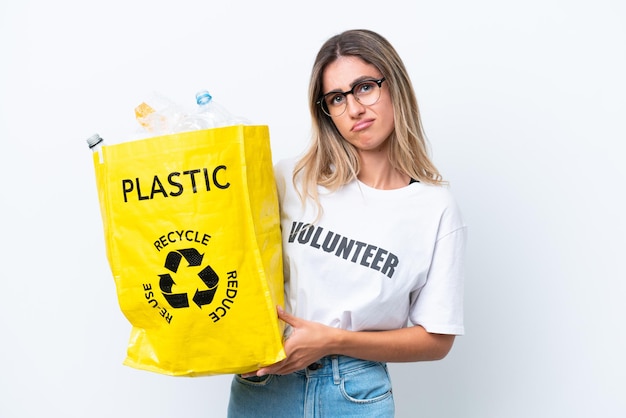 Young pretty Uruguayan woman holding a bag full of plastic bottles to recycle isolated on white background with sad expression