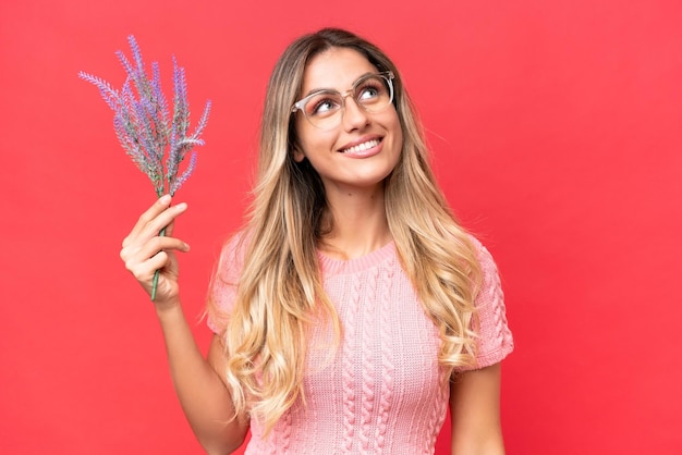 Young pretty Uruguayan woman holding lavender isolated on red background looking up while smiling