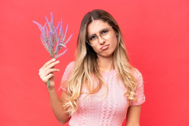 Young pretty Uruguayan woman holding lavender isolated on red background with sad expression