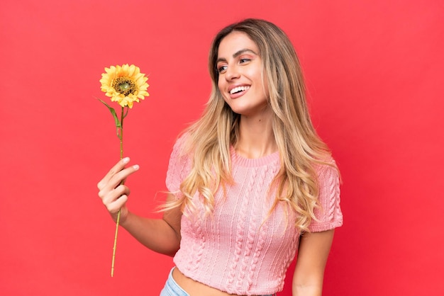 Young pretty Uruguayan woman holding sunflower isolated on background with happy expression