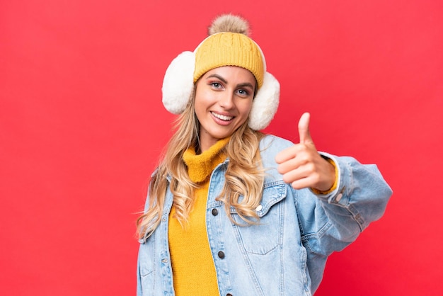 Young pretty Uruguayan woman wearing winter muffs isolated on red background background with thumbs up because something good has happened