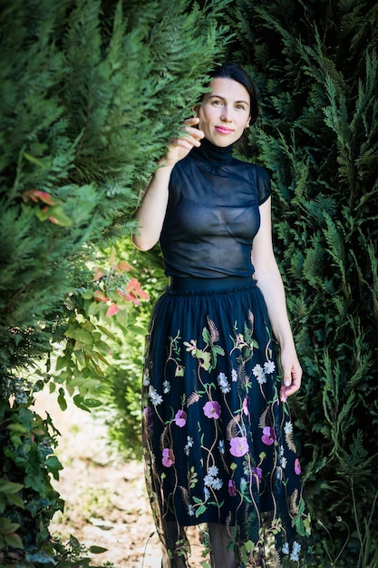 A young pretty woman in black clothes is standing near a bush