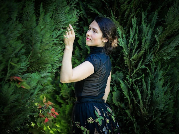 A young pretty woman in black clothes is standing near a bush