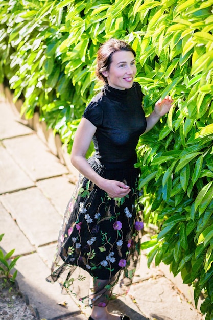 A young pretty woman in black clothes standing near a bush in a backyard