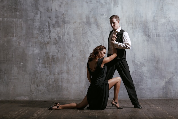 Young pretty woman in black dress and man dance tango