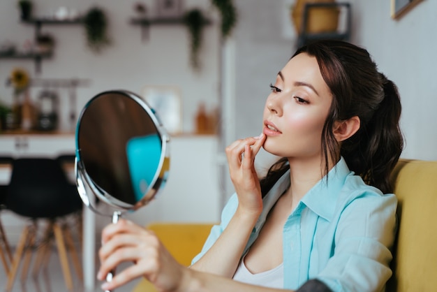 Young pretty woman does makeup at home while looking in the mirror