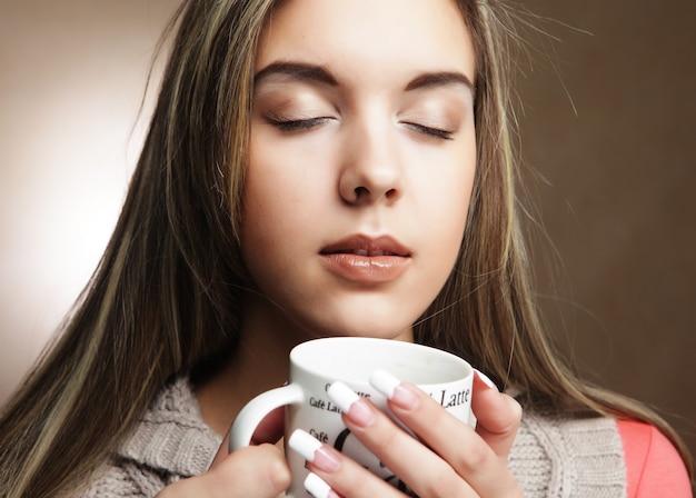 Young pretty woman drinking coffee over beige background