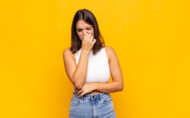 Young pretty woman feeling disgusted, holding nose to avoid smelling a foul and unpleasant stench