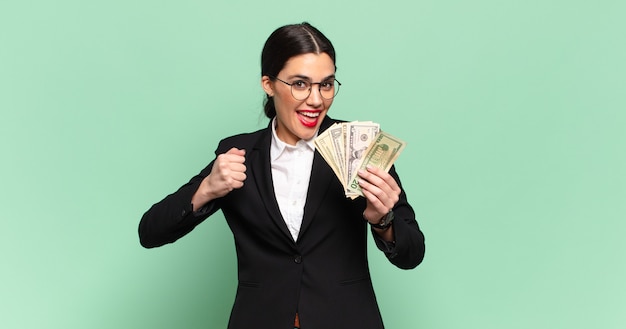 Young pretty woman feeling happy, positive and successful, motivated when facing a challenge or celebrating good results. business and banknotes concept