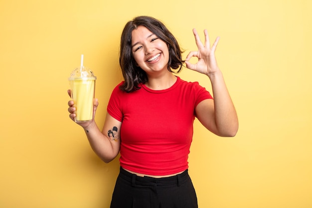 Young pretty woman feeling happy, showing approval with okay gesture. milkshake concept