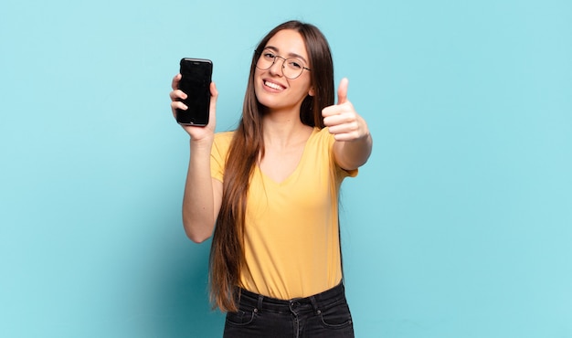 Young pretty woman feeling proud, carefree, confident and happy, smiling positively with thumbs up