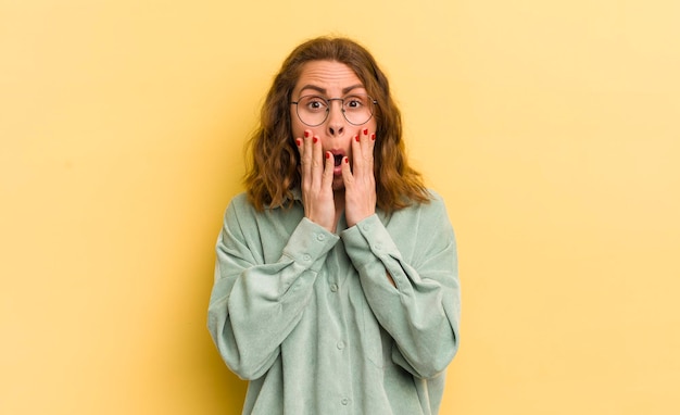 Young pretty woman feeling shocked and scared looking terrified with open mouth and hands on cheeks