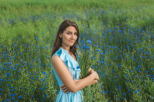 Young pretty woman among the field of beautiful cornflowers