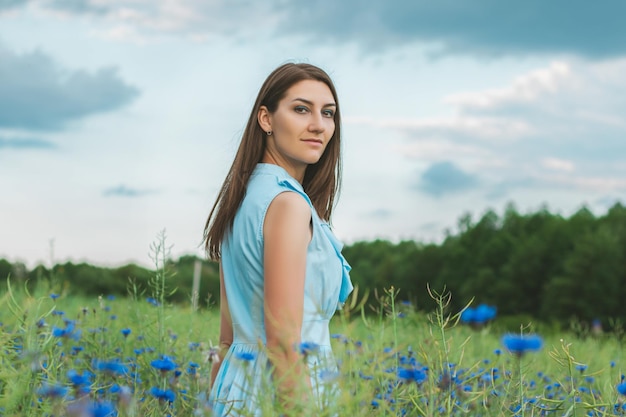 Young pretty woman among the field of beautiful cornflowers