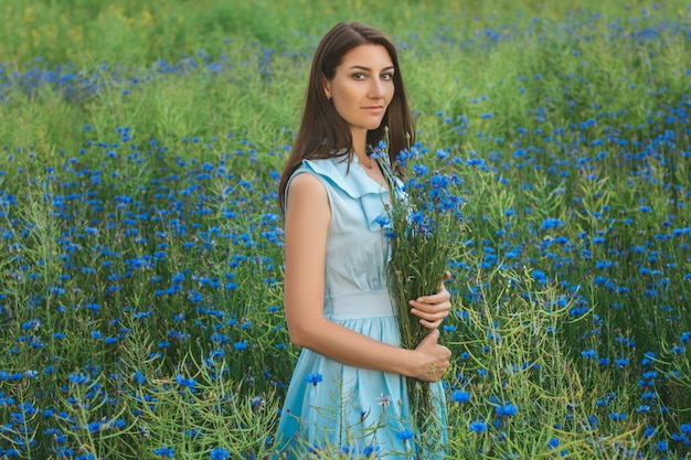 Young pretty woman among the field of beautiful cornflowers