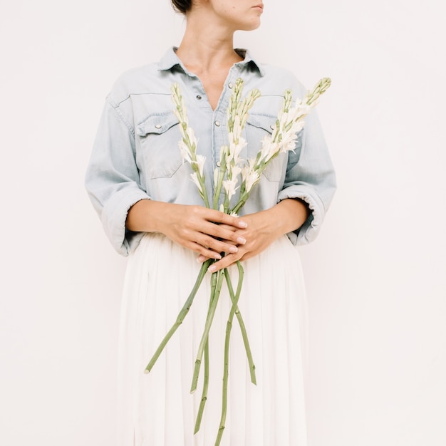 Young pretty woman holding bouquet of white flowers near white wall.