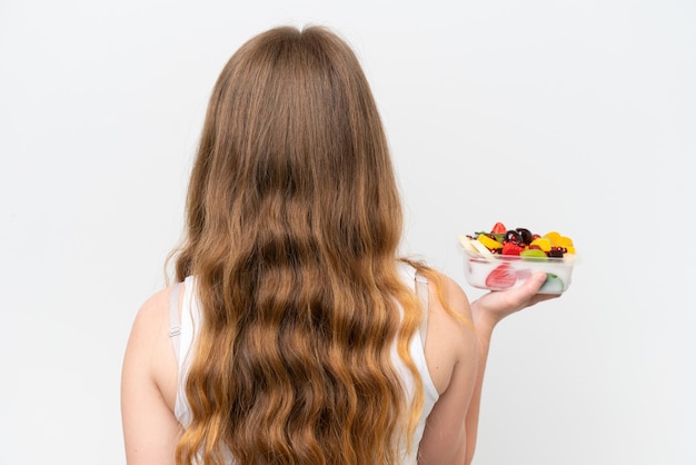 Young pretty woman holding a bowl of fruit isolated on white background in back position