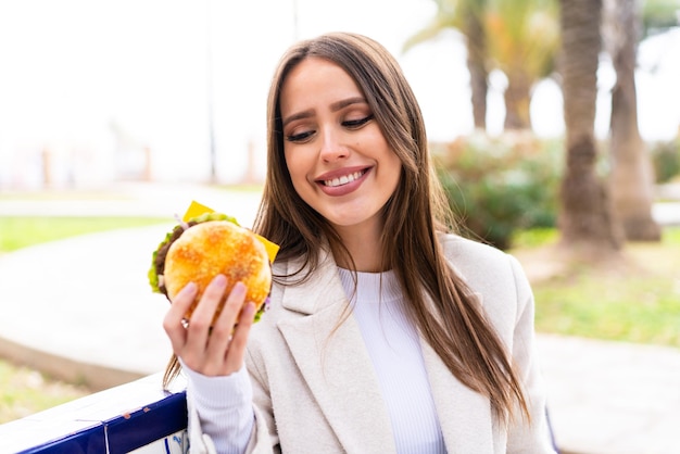 Young pretty woman holding a burger at outdoors with happy expression