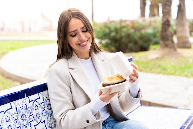 Young pretty woman holding a burger at outdoors