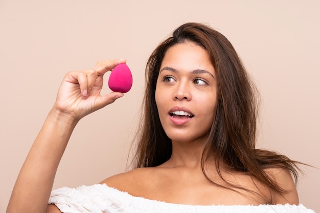 Young pretty woman holding cosmetics over isolated wall