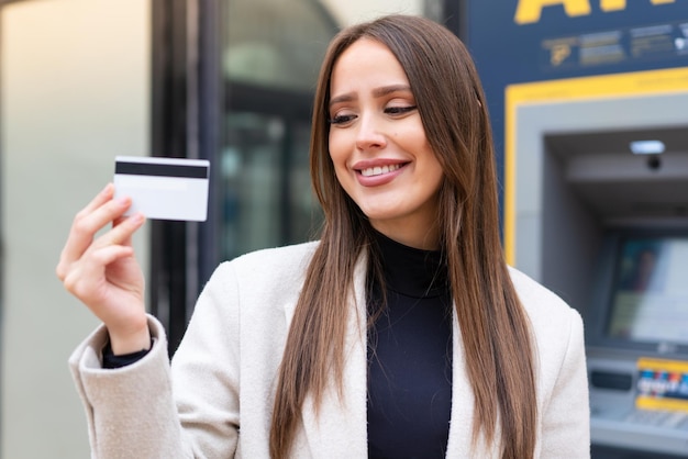 Young pretty woman holding a credit card at outdoors with happy expression