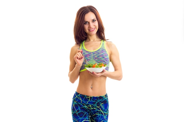 Young pretty woman holding a fork and white plate with green salad and tomato on white background