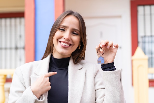 Young pretty woman holding home keys at outdoors with surprise facial expression