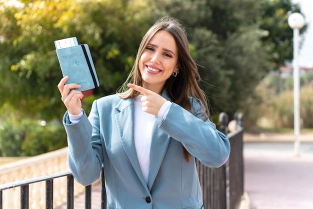 Young pretty woman holding a passport at outdoors and pointing it