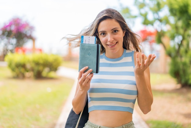 Young pretty woman holding a passport at outdoors with shocked facial expression