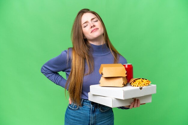 Young pretty woman holding pizzas and burgers over isolated chroma key background suffering from backache for having made an effort