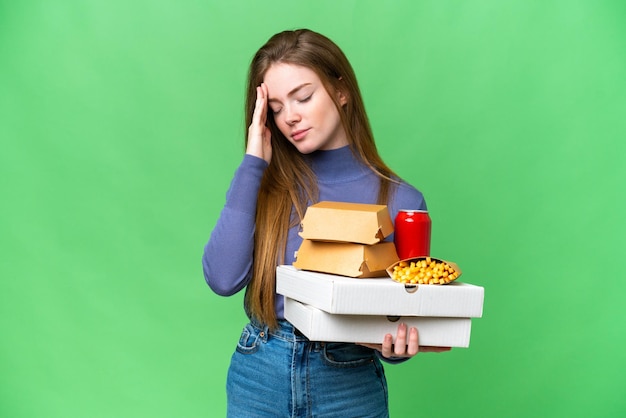 Young pretty woman holding pizzas and burgers over isolated chroma key background with headache