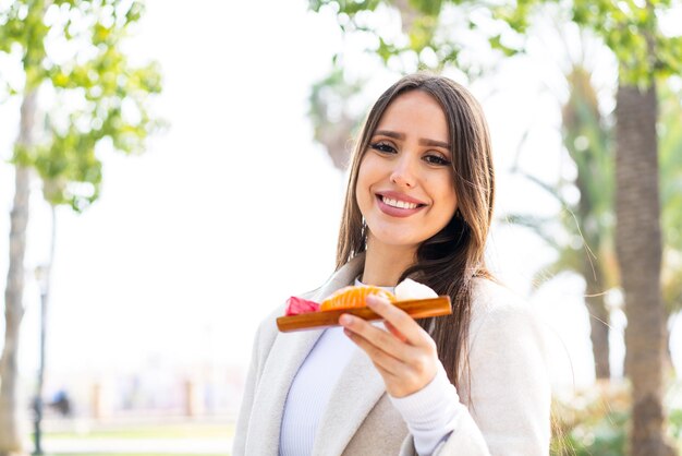 Young pretty woman holding sashimi at outdoors smiling a lot