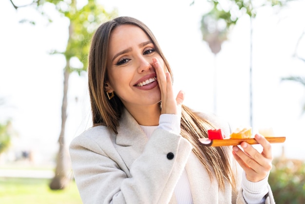 Young pretty woman holding sashimi at outdoors whispering something