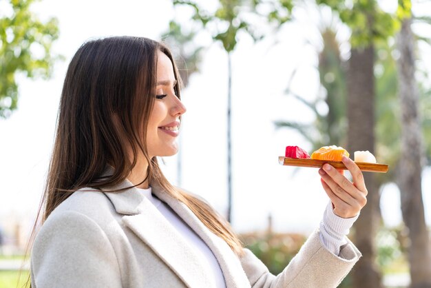 Young pretty woman holding sashimi at outdoors with happy expression