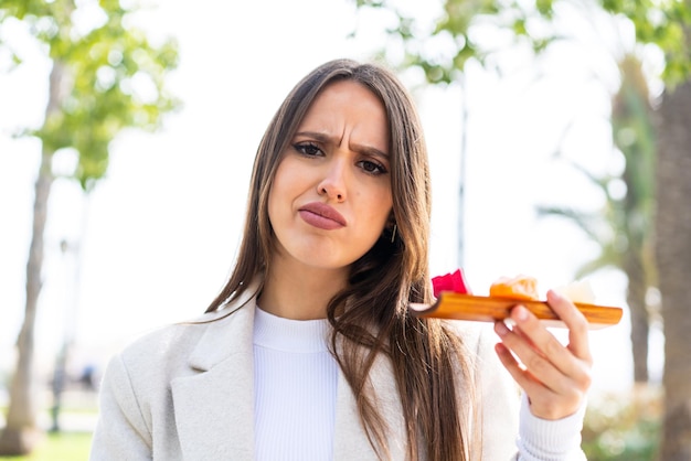 Young pretty woman holding sashimi at outdoors with sad expression