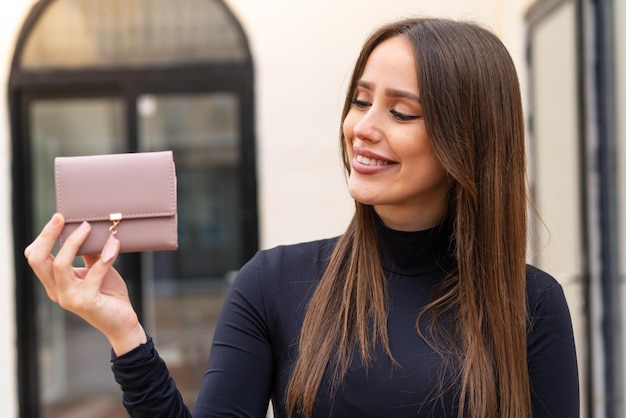 Young pretty woman holding a wallet at outdoors with happy expression