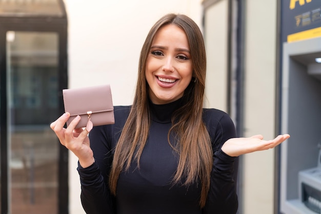 Young pretty woman holding a wallet at outdoors with shocked facial expression