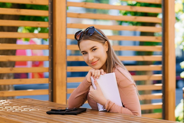 Young pretty woman holds a notebook in her hands and sits at a table in a street cafe or a cavorting