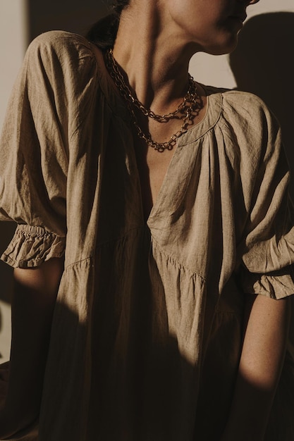 Young pretty woman in linen dress and golden necklace against wall Aesthetic silhouette in sun light Sunlight shadows shades on the wall Elegant minimal fashion design concept