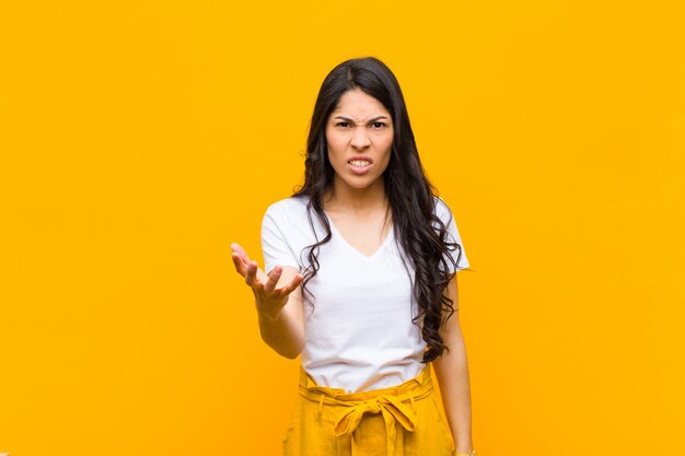 Young pretty woman looking angry, annoyed and frustrated screaming wtf or whatÃ¢ÂÂÃÂÃÂ´s wrong with you against orange wall