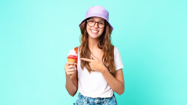 Young pretty woman looking excited and surprised pointing to the side holding an ice cream. summer concept