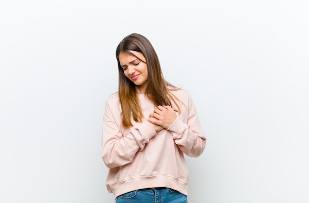 Young pretty woman looking sad, hurt and heartbroken, holding both hands close to heart, crying and feeling depressed against white background