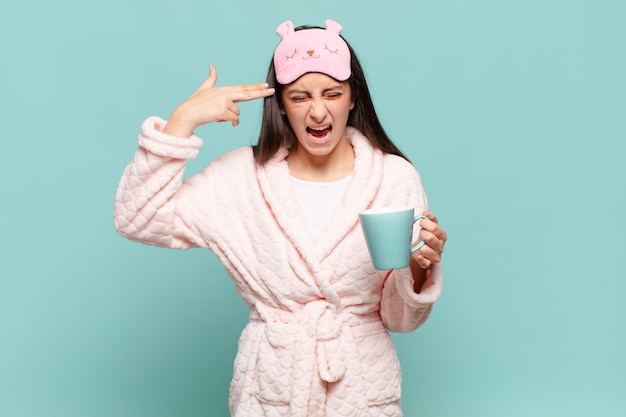 Young pretty woman looking unhappy and stressed, suicide gesture making gun sign with hand, pointing to head. awaking wearing pajamas concept