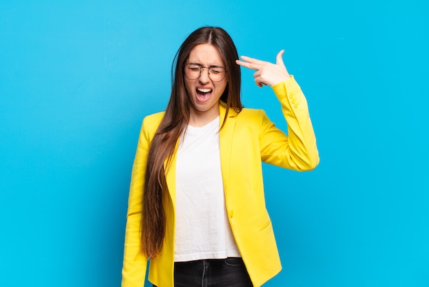 Young pretty woman looking unhappy and stressed, suicide gesture making gun sign with hand, pointing to head